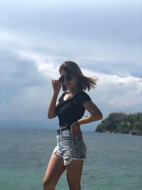 Portrait of young woman standing against sea and sky