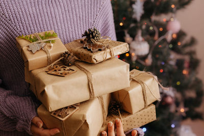 Closeup of woman in violet pullover holding many gift boxes in her hands. decorated christmas tree