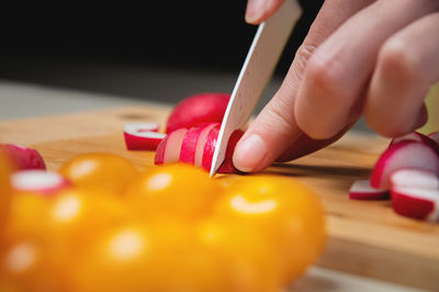 Close-up of female hands cut fresh raw radish on a wooden board against the background of yellow