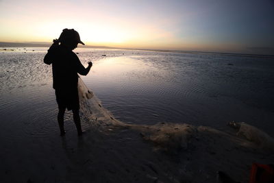 Silhouette man on beach against sky during sunset