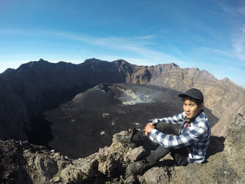 Full length of man sitting on rock against sky