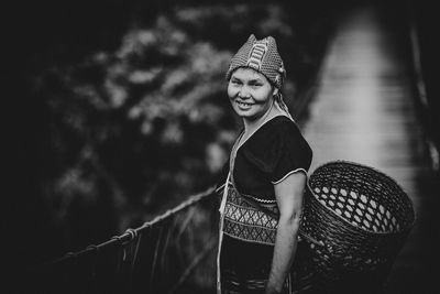 Portrait of smiling woman carrying basket while standing on footbridge