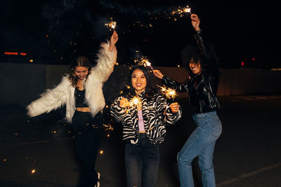 Smiling women holding sparkler dancing outdoors