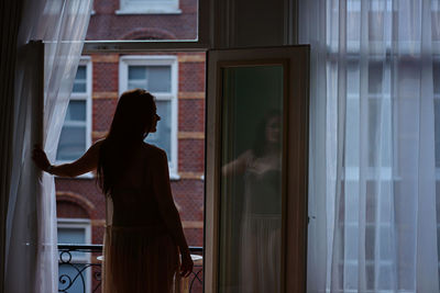 Rear view of woman looking through window at home