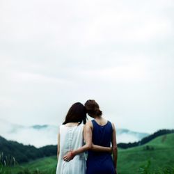 Rear view of female friends standing on field against sky