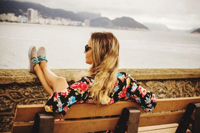 Woman leaning on bench against sea