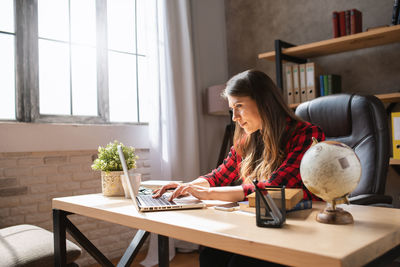 Young woman using phone while sitting on table at home