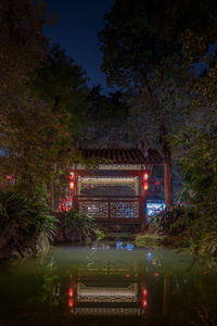 Illuminated building by lake against sky at night