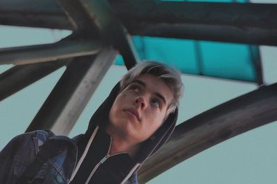 Low angle view of young man wearing hooded shirt below bridge