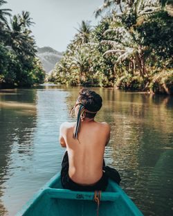 Rear view of shirtless man sailing in lake against trees