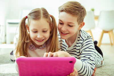 Siblings using digital tablet while lying at home