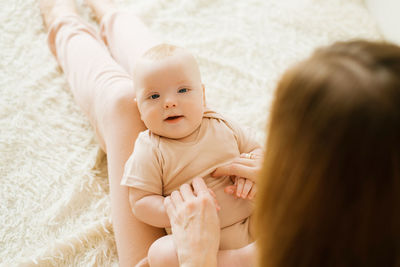 Newborn boy lies on his mother's lap and looks, the mother holds his hands