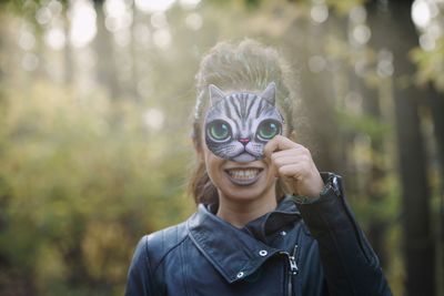 Smiling young woman holding mask in forest