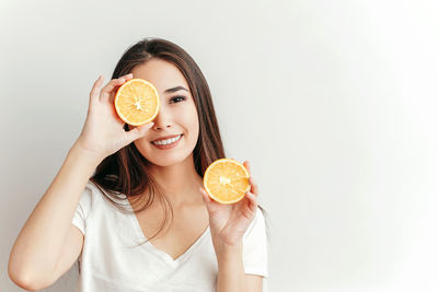 Portrait of a smiling young woman holding apple against white background