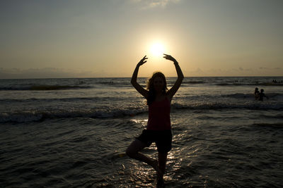 Woman standing at beach against sky during sunset