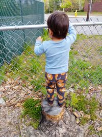 Rear view of boy standing by chainlink fence