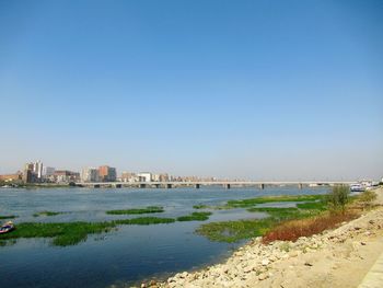 Scenic view of sea by buildings against clear blue sky