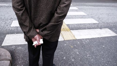 Midsection of man standing on road by zebra crossing 