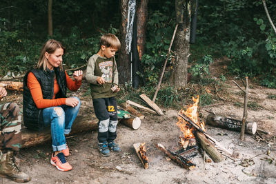 Mom and son are sitting by the fire during a family vacation. camping in the forest