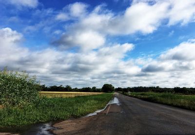 Empty road amidst field against sky