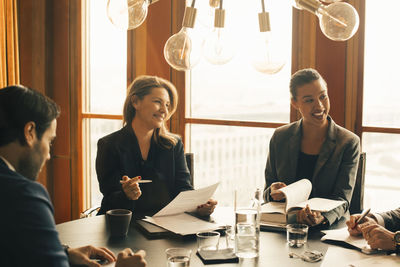 Smiling male and female legal professionals discussing on documents at meeting in office