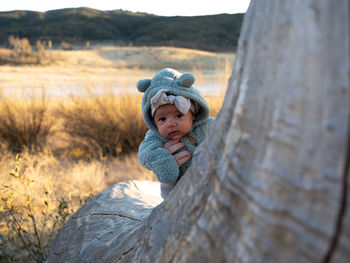 Portrait of cute baby girl behind tree trunk