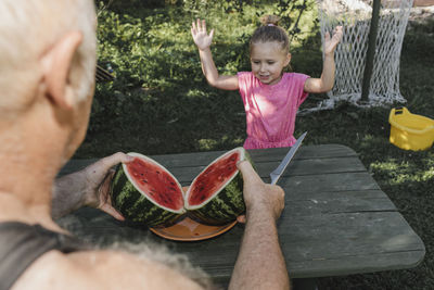 Portrait of little girl in the garden with her grandfather slicing watermelon