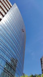 Low angle view of workers cleaning modern office building against clear blue sky