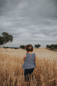 Rear view of baby girl standing on land against sky