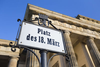 Low angle view of road sign against clear blue sky