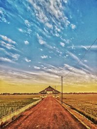 Road amidst field against sky during sunset