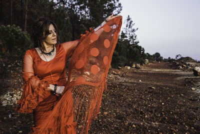 Woman holding fabric while standing on land against sky