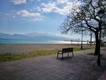 Empty bench by lake against sky