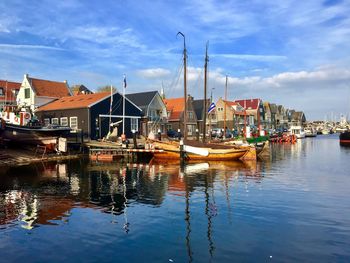 Sailboats moored on river by buildings against sky