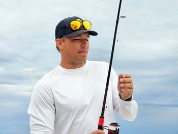 Rear view of man holding fishing rod against sky