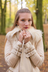 Portrait of young beautiful woman wearing jacket against autumn trees