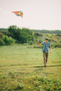 Full length of man flying kite on grassy field against sky