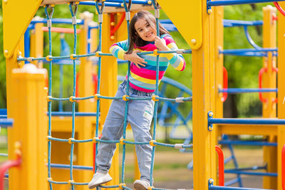 Little cute girl 5-6 years old stands on a rope ladder, on a childrens ladder on a bright playground