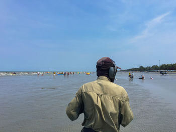 Rear view of guard standing at beach against sky