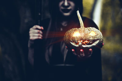Midsection of woman in witch costume holding illuminated jack o lantern