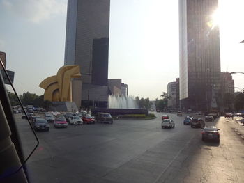 Traffic on road by buildings in city against sky