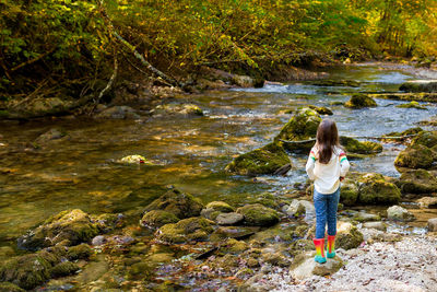 Rear view of girl standing on rock by stream
