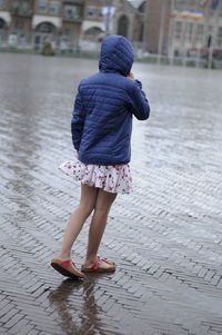 Rear view of girl wearing raincoat walking on wet road