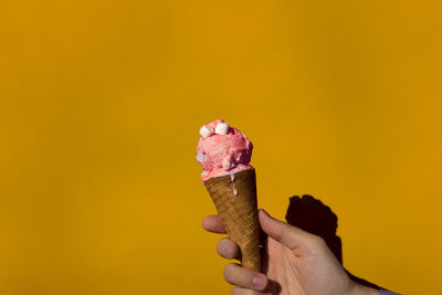 Cropped hand holding ice cream against yellow wall on sunny day