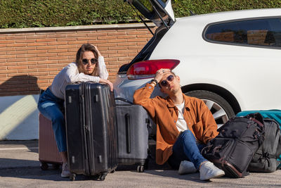 Man and woman sitting on the floor tired and desperate with the luggage in the car trunk