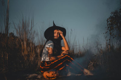 Woman wearing hat while standing on land against sky at sunset