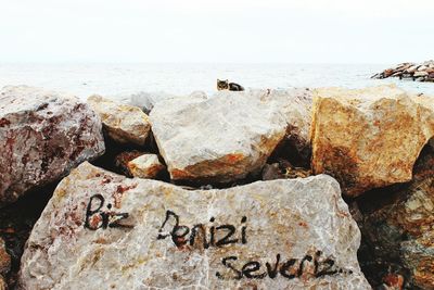 Text on rock by sea against sky