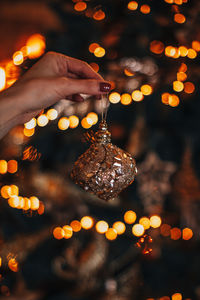 Female hand holding golden christmas ball against a background of festive golden bokeh lights