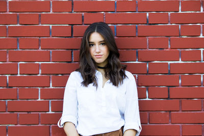 Portrait of beautiful young woman standing against brick wall