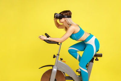 Low section of woman exercising on exercise mat against yellow background